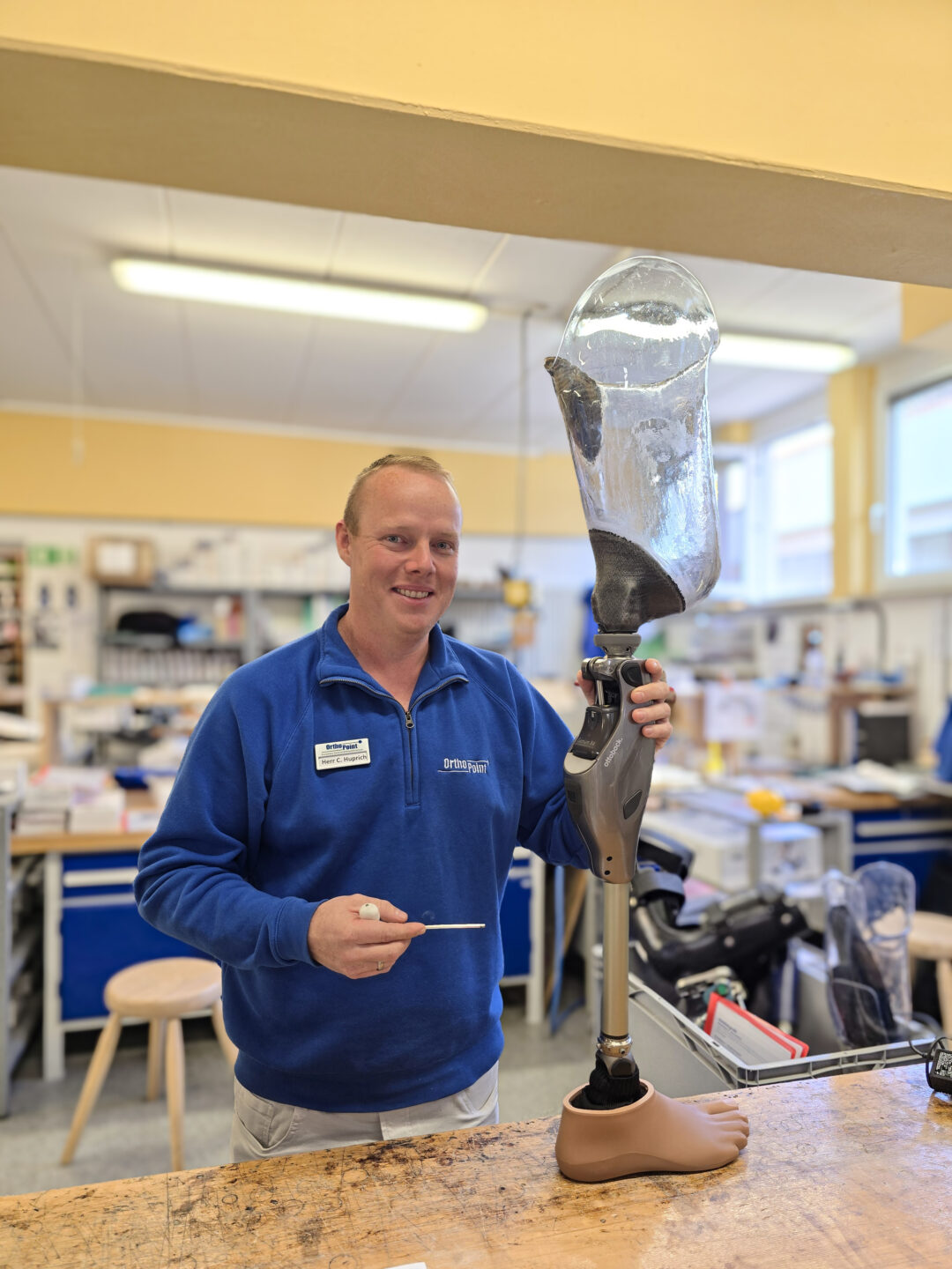 Orthopädietechniker hält eine Prothese in der Hand und ein Werkzeug und steht in der Werkstatt