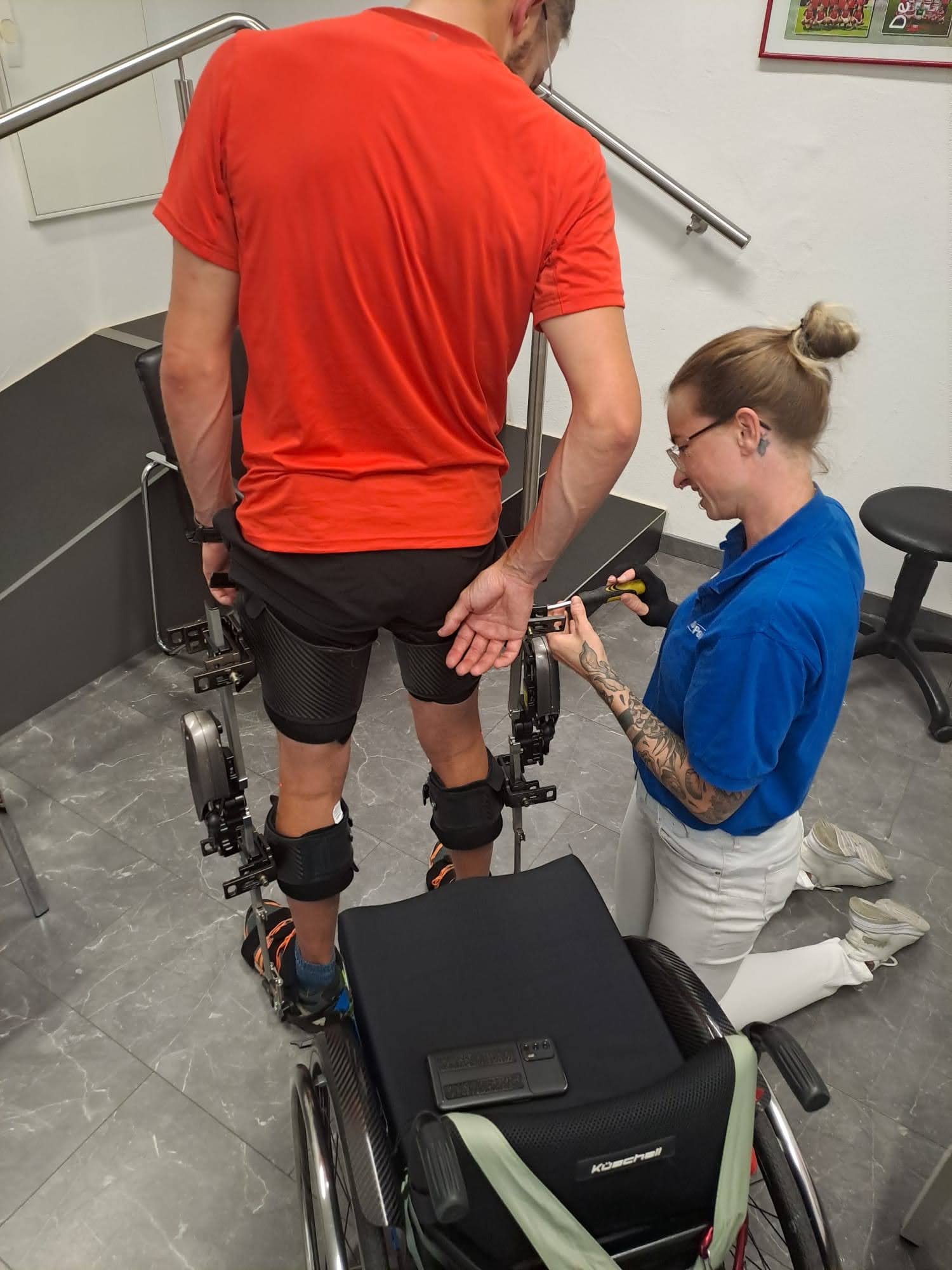 Orthopädietechnikerin passt Beinorthesen bei einem Patienten mit einem roten T-Shirt an