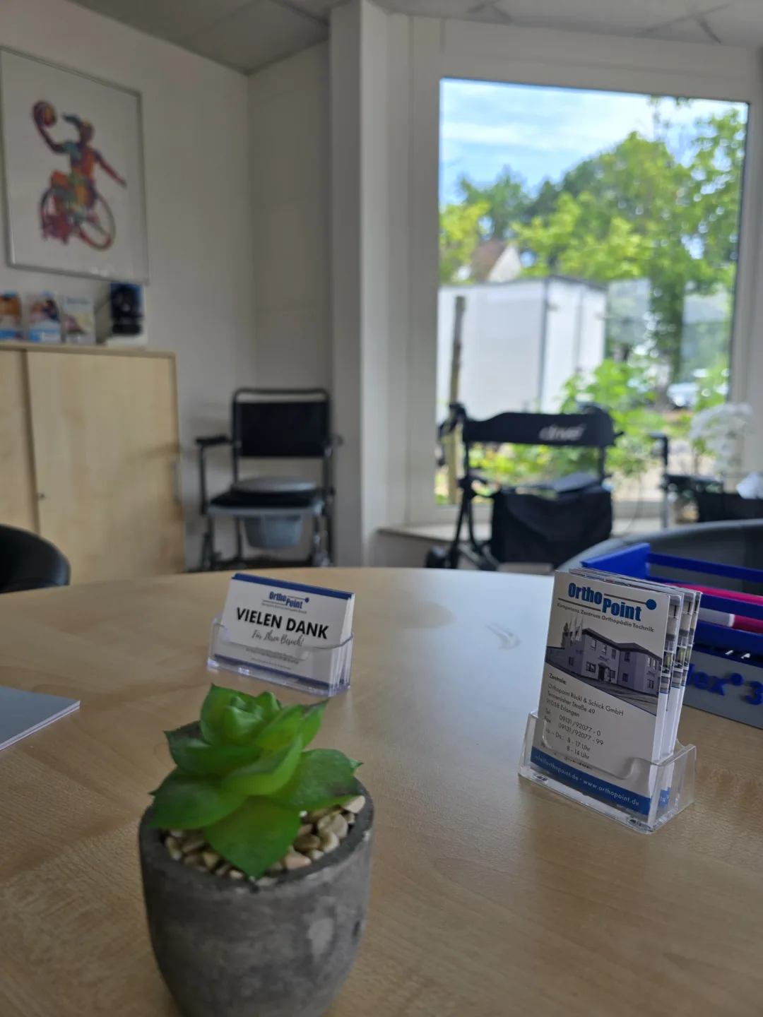 OrthoPoint Visitenkarte auf einem Tisch im Hintergrund ein Fenster und Vegetation.