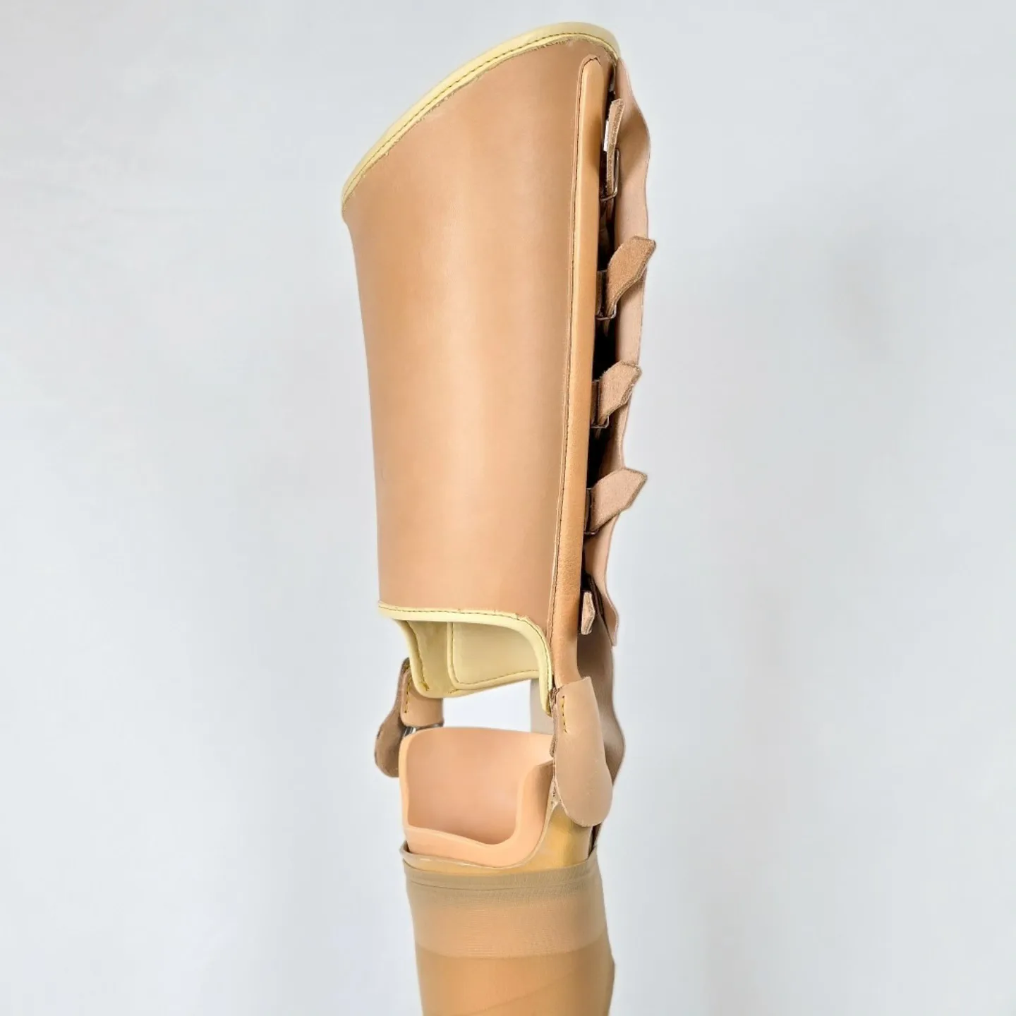 Ganzbeinorthese aus hellem Leder von hinten zu sehen vor hellem Hintergrund.