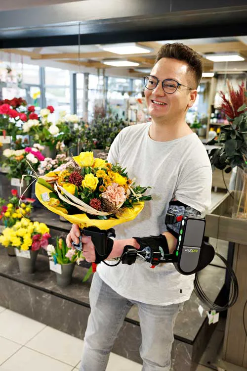 Junger Mann mit einem Blumenstrauß in der Hand der eine MyoPro Arm- und Handorthese trägt